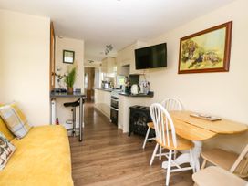 A kitchen area with a wooden table and chairs a sofa and a wall-mounted TV at Poppy in Raglan