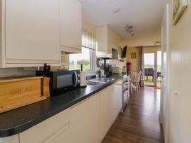 A kitchen with white cabinets black countertop a microwave bread box knife block and a dining table with chairs near glass doors at Poppy in Raglan