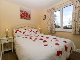 A bedroom with a double bed with floral bedding and nightstands with lamps at Poppy in Raglan