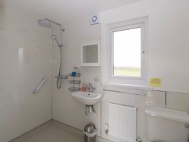 A bathroom with a shower, sink, toilet, window, wall-mounted mirror cabinet, radiator, grab bar, and trash can at Poppy in Raglan
