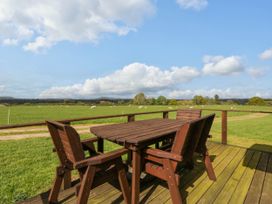 A wooden outdoor table with chairs on a deck overlooking a green field with sheep at Poppy in Raglan