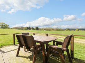 A wooden table with four chairs on a deck overlooking a green field with trees and clouds at Poppy in Raglan