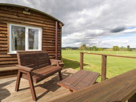 A wooden bench and table on a deck outside a wooden cabin overlooking a green field at Poppy in Raglan