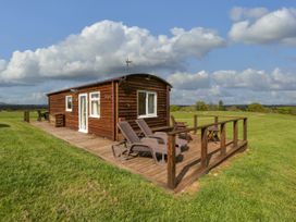 A wooden cabin with deck chairs and a table on a grassy field at Poppy in Raglan