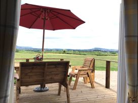 A wooden deck with a bench, chair, table, red umbrella, and flowers overlooking a green field at Poppy in Raglan