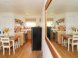 A kitchen with a black refrigerator a wooden dining table and chairs and orange checkered backsplash at Number 24 The Park in Kilkhampton
