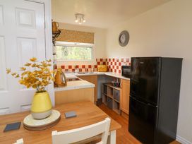 A kitchen with a wooden table and yellow vase with flowers a black fridge and orange checked backsplash at Number 24 The Park in Kilkhampton