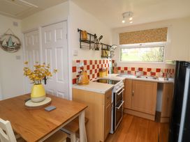 A kitchen with wooden cabinets a wooden dining table with a yellow vase on top and a window with a patterned blind at Number 24 The Park in Kilkhampton
