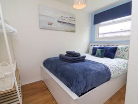 A small bedroom with a bed with blue and floral bedding towels on the bed artwork on the wall and a shelving unit with baskets at Number 24 The Park Kilkhampton
