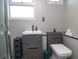 A bathroom with a shower, a sink with a cabinet, a toilet, and storage baskets at Number 24 The Park in Kilkhampton