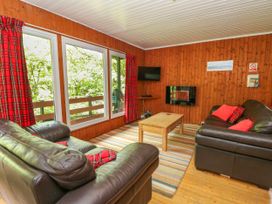 A living room with two black leather sofas a wooden coffee table and large windows with red plaid curtains at Lodge 2 - Rowan in Glenkiln near Lamlash