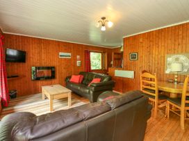 A living room with wooden walls two leather sofas a wooden coffee table a dining table with chairs and a wall-mounted TV at Lodge 2 - Rowan in Glenkiln near Lamlash