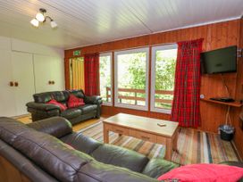 A living room with leather sofas a wooden table a TV on the wall and large windows with red curtains at Lodge 2 - Rowan in Glenkiln near Lamlash