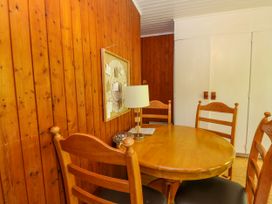 A wooden dining table with four chairs a lamp and a framed artwork on a wooden wall at Lodge 2 - Rowan in Glenkiln near Lamlash