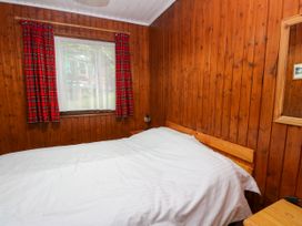 A bedroom with wood-paneled walls a bed with white bedding red check curtains and a window at Lodge 2 - Rowan in Glenkiln near Lamlash