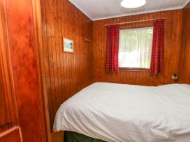 A bedroom with a white bedspread a window with red plaid curtains and wood paneled walls at Lodge 2 - Rowan in Glenkiln near Lamlash