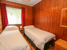 A bedroom with two single beds a nightstand with a lamp red curtains wooden walls and a wooden dresser with a mirror at Lodge 2 - Rowan in Glenkiln near Lamlash
