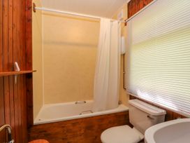 A bathroom with a bathtub with shower curtain a toilet and a window with blinds at Lodge 2 - Rowan in Glenkiln near Lamlash