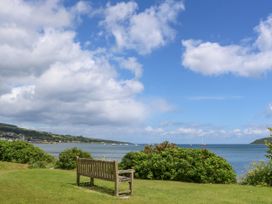 A wooden bench on grass overlooking a body of water with boats and shrubs in Glenkiln near Lamlash