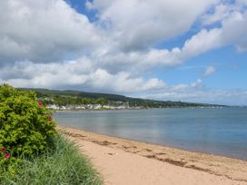 A sandy beach with grassy bushes beside a calm body of water and houses on the far shore at Lodge 2 - Rowan in Glenkiln near Lamlash