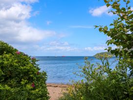 A beach with green bushes and flowers by the sea with sailboats in the distance at Lodge 2 - Rowan in Glenkiln near Lamlash