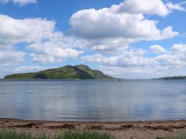 A sandy beach with grass in the foreground a body of water with boats and an island under a sky with clouds at Lodge 2 - Rowan in Glenkiln near Lamlash