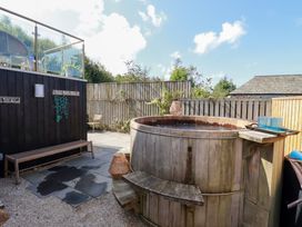 A garden with a wooden hot tub and seating area at Stable Loft Watergate Bay