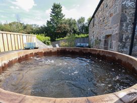 A hot tub on a wooden deck with a stone wall and plants at Stable Loft Watergate Bay