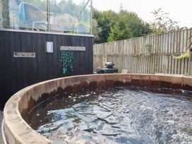 A hot tub surrounded by wooden deck and garden features at Stable Loft in Watergate Bay