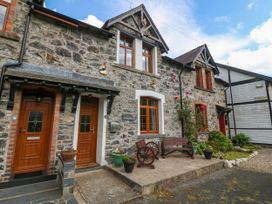 Front view of a stone house with wooden doors and windows a small porch with benches potted plants and butterflies on the wall at Ty Pili Pala in Betws-Y-Coed