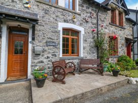 A stone exterior house with wooden door two wooden benches flower pots and garden at Ty Pili Pala in Betws Y Coed