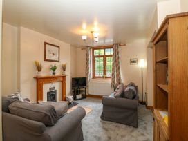 A living room with gray sofas a wooden fireplace a TV on a stand a wooden bookshelf and a window with patterned curtains at Ty Pili Pala in Betws-Y-Coed