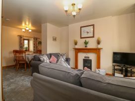 A living room with gray sofas a fireplace and a television and a dining area with wooden chairs at Ty Pili Pala in Betws-Y-Coed