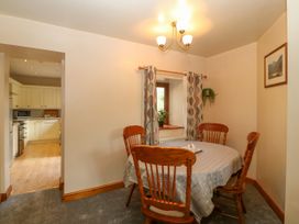 A dining room with a table covered with a cloth and four wooden chairs next to a window with curtains and a small plant in Betws-Y-Coed