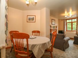 A dining area with wooden chairs and tablecloth next to a living room with sofas and window at Ty Pili Pala in Betws Y Coed