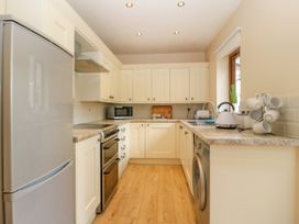 A kitchen with white cabinets wooden floor a refrigerator stove microwave washing machine and a window at Ty Pili Pala in Betws-Y-Coed
