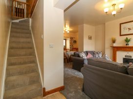A carpeted staircase next to a living room with sofas dining table and chairs with a fireplace at Ty Pili Pala in Betws-Y-Coed
