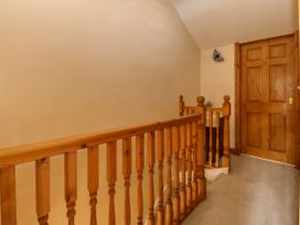 A hallway with wooden railing and a wooden door with beige walls and carpeted floor at Ty Pili Pala in Betws-Y-Coed