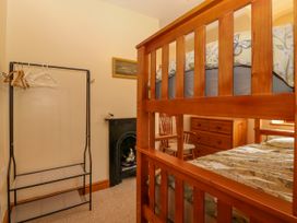 A bedroom with a wooden bunk bed a black metal clothes rack a cushioned wooden chair a wooden chest of drawers and a small black fireplace with a stuffed dog at Ty Pili Pala in Betws-Y-Coed