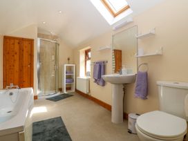A bathroom with a bathtub shower unit pedestal sink toilet and shelves with towels at Ty Pili Pala in Betws-Y-Coed