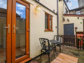 A small patio with two black metal chairs and a table near wooden framed glass doors and a small window at Ty Pili Pala in Betws-Y-Coed