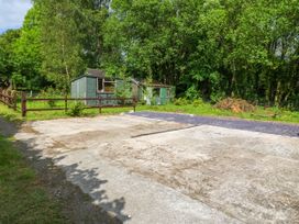 A paved driveway with two green sheds and trees in the background at Ty Pili Pala in Betws-Y-Coed