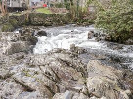 A flowing river with large rocks and a stone wall alongside a residential area at Ty Pili Pala in Betws-Y-Coed