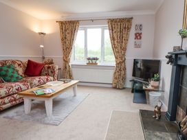 A living room with a patterned sofa cushions a coffee table near a window with curtains a television on a glass stand and a fireplace at 2 Mountain View in Chirk
