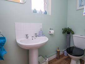 A bathroom with a pedestal sink a toilet with a black seat a toilet paper holder and small window with decorative items at 2 Mountain View in Chirk