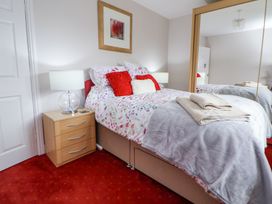 A bedroom with a bed with floral bedding and red pillows a wooden bedside table with a lamp and a mirrored wardrobe at 2 Mountain View in Chirk