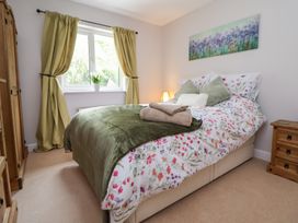 A bedroom with a bed covered in floral bedding and green pillows a wooden wardrobe and nightstand near a window with curtains and a flower pot at 2 Mountain View in Chirk