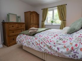 A bedroom with a floral bedspread a wooden dresser and wardrobe and green curtains at 2 Mountain View in Chirk