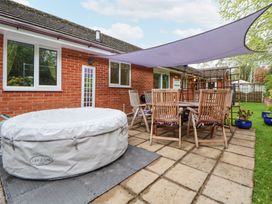 An outdoor patio with a covered hot tub wooden chairs around a table and a shade sail at 2 Mountain View in Chirk