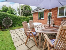 An outdoor patio with a wooden table and chairs a hanging chair and a hot tub next to a brick house at 2 Mountain View in Chirk